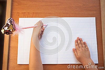 A child writes in an empty notebook on a wooden desk background. Back to school concept. Top view Stock Photo