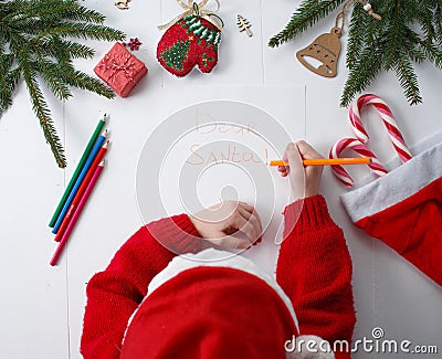 Child writes the letter to Santa Claus. Child`s hands, the sheet of paper, pencils and Christmas decorations on a wooden surface. Stock Photo