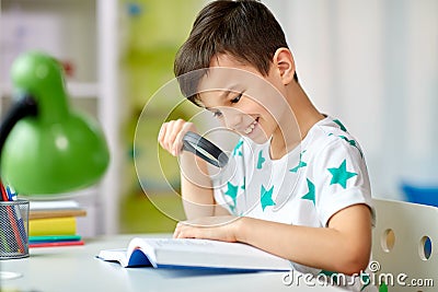 Boy with magnifier reading book at home Stock Photo