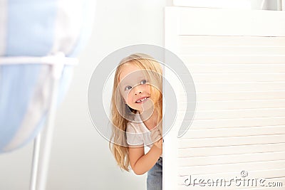 Childhood, fun and people concept - happy smiling beautiful little girl hiding behind room door. The child plays hide and seek at Stock Photo