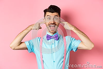 Childish funny guy shut ears and laughing at camera, refuse to listen, standing ignorant on pink background Stock Photo