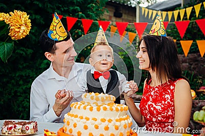 Children birthday theme. family of three Caucasian people sitting in backyard of the house at a festive decorated table in funny h Stock Photo