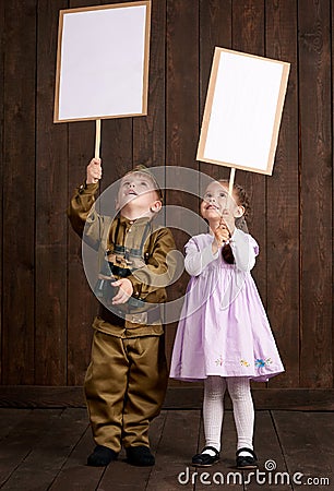 Children boy are dressed as soldier in retro military uniforms and girl in pink dress. They`re holding blank posters for veterans Stock Photo