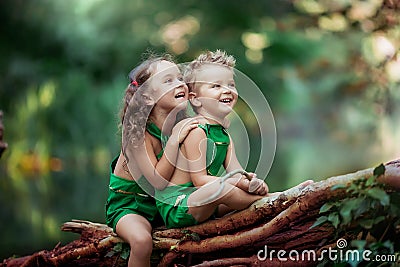 Children a boy and a girl in the forest near a fabulous green lake sitting on a fallen tree Stock Photo