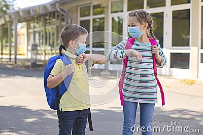 Children, a boy and a girl, wearing masks, greet their elbows on the street in the schoolyard due to the coronavirus epidemic. Stock Photo