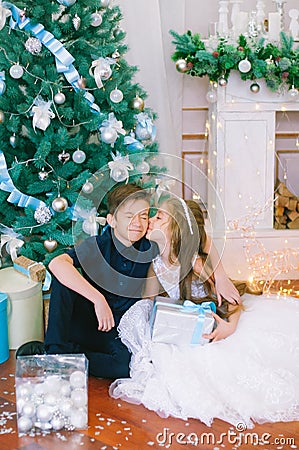 Children, a boy and a girl in a white ball gown near a Christmas tree in holiday dresses with gifts and silver confetti. Stock Photo