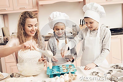 Children with mother in kitchen. Mother is putting dough in baking dish and kids are adding raisins. Stock Photo