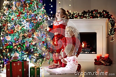 Children at Christmas tree. Kids at fireplace on Xmas eve Stock Photo