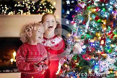 Children at Christmas tree. Kids at fireplace on Xmas eve Stock Photo