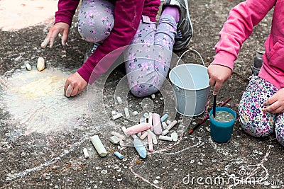 Children drawing with chalk on the concrete sitting on the ground. Art therapy, CBT, simple creativity excercises. Two girls Stock Photo