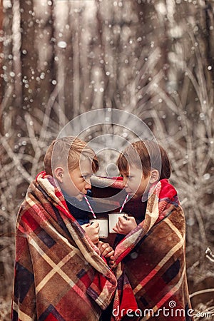 Children drink hot chocolate under warm blanket in winter forest. Christmas vacation. Stock Photo