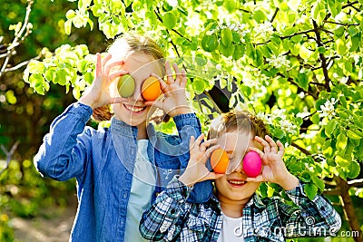 Children on an Easter egg hunt in a blooming spring garden. Toddler boy and preschool girl play in the open air. They put their Stock Photo