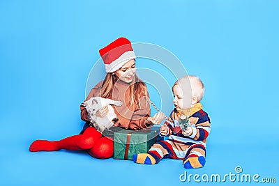 Children in front of a blue background. Box in green packaging with a gift. A child holds a cat in his hands, a boy holds a small Stock Photo