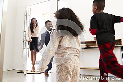 Children Greeting And Hugging Working Parents As They Return Home From Work Stock Photo