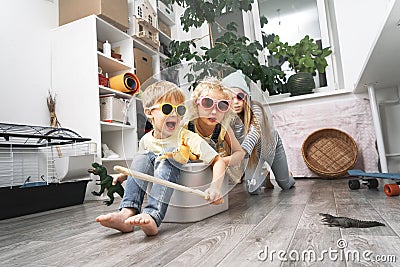 Children have fun and ride in a white plastic box. The room is a mess. Stock Photo