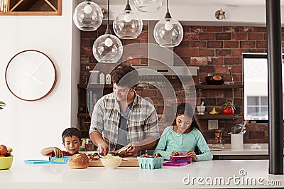Children Helping Father To Make School Lunches In Kitchen At Home Stock Photo