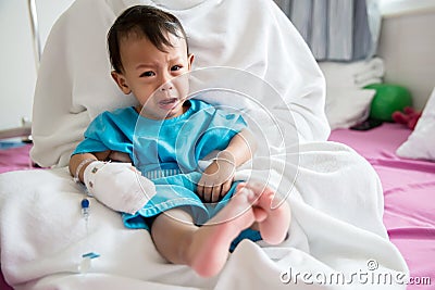 Children illness . Little Baby attaching intravenous tube to patient`s hand in hospital bed. Baby sick and crying on mom . Stock Photo