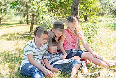 Children learn in nature, four children read a book in the park in the open air. Pupils are preparing for school Stock Photo
