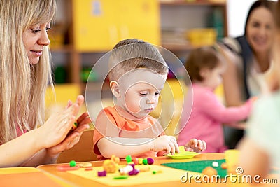 Children at lesson in kindergarten. Baby toddler playing with plasticine with teacher in nursery playroom. Stock Photo
