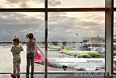 Children look out the big window at the planes in the airport building Editorial Stock Photo