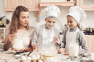 Children with mother in kitchen. Kids are adding flour and mother is adding milk in bowl. Stock Photo