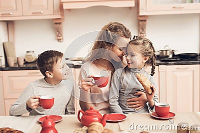 Children with mother in kitchen. Family is drinking tea with croissants. Stock Photo