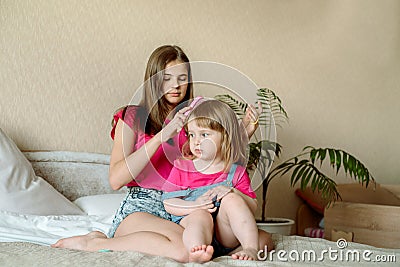 Children play on the bed in a bright bedroom. teen girl combing baby hair. funny girls. sisterly love. vacation home Stock Photo