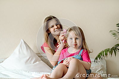 Children play on the bed in a bright bedroom. teen girl combing baby hair. funny girls. sisterly love. vacation home Stock Photo