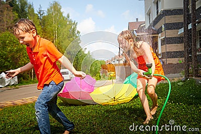 Children playing with garden sprinkler. Brother and sister running and jumping. Summer outdoor water fun in backyard Stock Photo