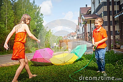 Children playing with garden sprinkler. Brother and sister running and jumping. Summer outdoor water fun in backyard Stock Photo