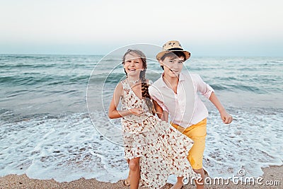 Children play and have fun on the beach. Romantic story on the seafront. The girl and the guy run away from the wave Stock Photo