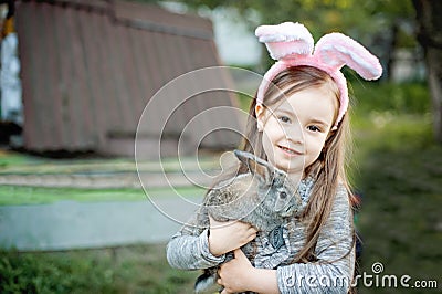 Children play with real rabbit. Laughing child at Easter egg hunt with white pet bunny. Little toddler girl playing with animal in Stock Photo