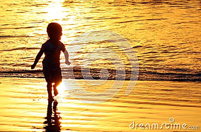 Children playing at the beach in Bali, Indonesia during a golden sunset. Ocean like gold. Stock Photo