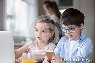 Children playing computer and smartphone while mother busy cooking breakfast Stock Photo