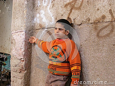 African boy child in the door village in an orange sweater posed against a stone background Editorial Stock Photo