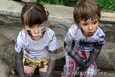 Children playing in mud, dirty cloth, messy face and hands in mud. Stains on clothes. Stock Photo