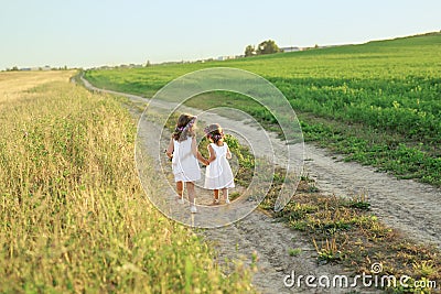 Children run hand in hand in the fresh air among fields and meadows on a narrow sandy path. Stock Photo