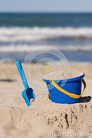 Children`s beach toys - bucket and shovel on sand on a sunny day. Outdoor kid`s activities at a beach with sea waves Stock Photo