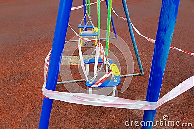 Children's blue swing on a sports playground in the park wrapped with red barrier tape Stock Photo