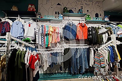 Children`s bright clothes hang on the display in the baby clothing store. Boys section Stock Photo