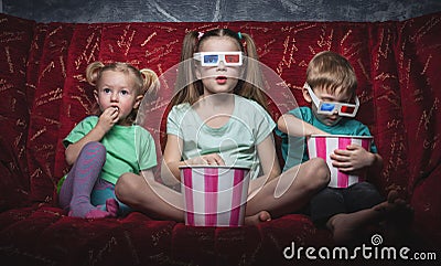 Children`s cinema: Children sit on a red sofa and watch a 3D movie. Stock Photo