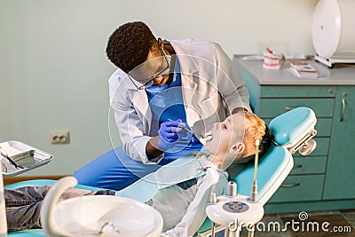 Children`s dentistry, Pediatric Dentistry. A male African-American stomatologist is treating teeth of a school-age boy Stock Photo