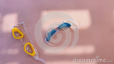 Children`s goggles for swimming on the trestle bed near the pool. Yellow and blue. The sun`s rays create a shadow picture Stock Photo