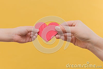 Children`s hand and the hand of a woman hold a red heart by the edges on a yellow background. The idea is peace, mutual Stock Photo