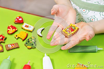 Children`s hands are holding a decorated rectangular cake. Colorful cinnamon cakes lie on the green table in the background. Tubes Stock Photo