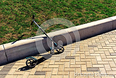 Children's scooter parked near the concrete curb. Outdoor Fun in the Summer Stock Photo