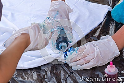 Children`s tie dye activity hands putting blue dye on a white shirt for creative artistic concepts Stock Photo