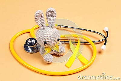 Children`s toy with a Childhood Cancer Awareness Golden Ribbon and stethoscope on yellow background Stock Photo