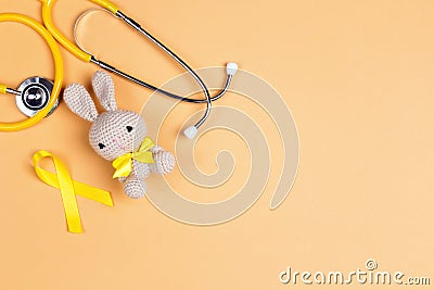 Children`s toy with a Childhood Cancer Awareness Golden Ribbon and stethoscope on yellow background with copy space Stock Photo