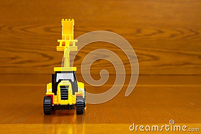 Children`s tractor yellow with a raised bucket on a brown background Stock Photo